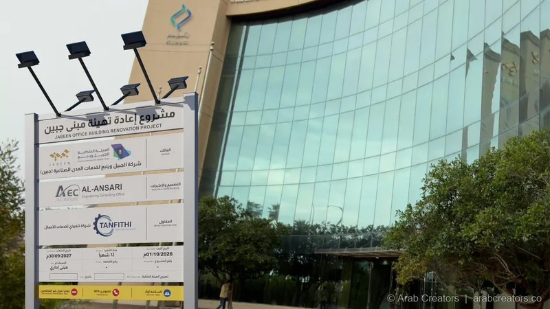لوحة مشروع على المسطح الأخضر أمام مبنى إداري بواجهة زجاجية
