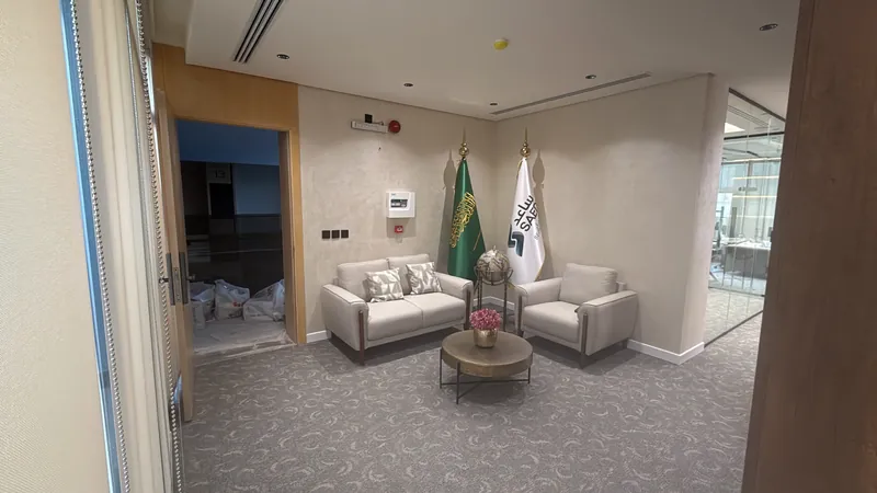 ركن استقبال بأريكة ومقعد منفرد وطاولة دائرية، بين جدران فاتحة بملمس جصي وأرضية موكيت